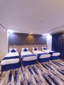 a room with four beds with blue and white pillows at فندق افاق المئوية للضيافة السياحي in Ash Shishah