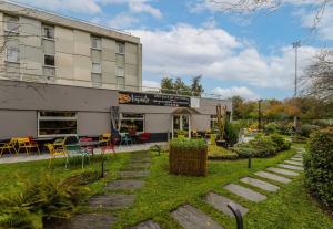 un bâtiment avec des tables et des chaises devant lui dans l'établissement B&B HOTEL Lille Villeneuve d'Ascq Grand Stade, à Villeneuve d'Ascq