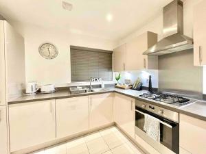 a kitchen with white cabinets and a clock on the wall at Hazel house new 4 bedroom home in Ashford in Ashford +15 photos