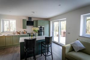 a kitchen with green cabinets and a bar with chairs at Padley; woodland lodge with hot tub for 2-4 in the Staffordshire Moorlands in Oakamoor