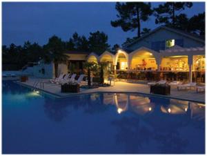 a swimming pool with chairs and a restaurant at night at Jolie Mobil home 103 in Saint-Jean-de-Monts