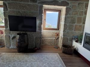 ein Wohnzimmer mit einem Fernseher an einer Steinwand in der Unterkunft Casa do Reguengo, Freigil in Resende