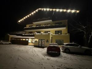 a house with two cars parked in the snow at night at Hotel Bergglück in Filzmoos