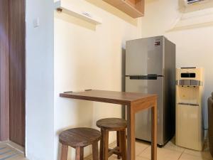 a kitchen with a table and two stools and a refrigerator at Warm and Homey 1BR at Belmont Residence Puri Apartment By Travelio in Jakarta