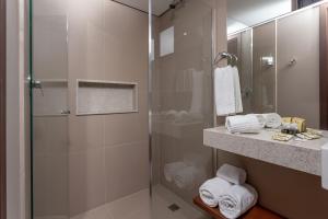 a bathroom with a shower and a sink with towels at Hotel Roochelle Convention By Nobile in Curitiba