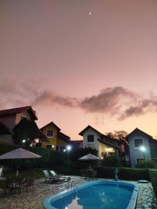 a pool with chairs and umbrellas at dusk at Linda casa de veraneio em Gravatá in Gravatá