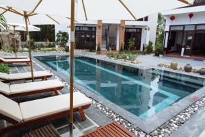 a pool with chairs and umbrellas next to a house at Hoi An Golden Rice Villa in Hoi An