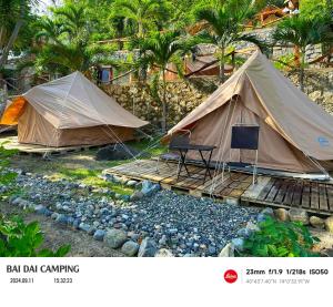 two tents with chairs and a boardwalk in front of trees at Bãi dài Camping in Nha Trang