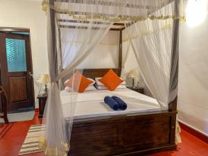 ein Schlafzimmer mit einem Himmelbett mit orangefarbenen und blauen Kissen in der Unterkunft Elmwon Heritage in Matara