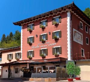 ein großes rotes Gebäude mit Leuten, die draußen sitzen in der Unterkunft Al Posta Hotel 1899 in Baselga di Pinè