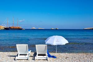 two chairs and an umbrella on a beach with a boat at Vrahos Boutique Hotel in Karavostasi