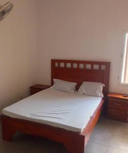a bedroom with a wooden bed with white sheets and pillows at Appartement chez Alioune in Tilel