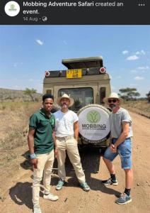 un grupo de tres hombres parados frente a un vehículo en Wildlife tour, en Arusha