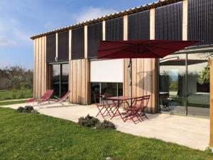 un patio avec une table, des chaises et un parasol rouge dans l'établissement Maison bioclimatique, à Meyrals