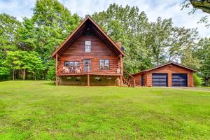 a log cabin on a grassy field with a house at Lovely Gilbertsville Cabin with Patio, 4 Mi to Water in Gilbertsville