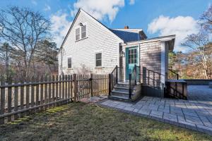 a white house with a wooden fence at Coastal Cape Cod Retreat by Barlows Landing Beach, Pergola, Firepit & Fenced Yard, Sleep 7 with Smart TVs & Eat-In Kitchen, Family-Friendly Escape Minutes to Old Silver Beach, Woods Hole & Downtown Falmouth in Bourne