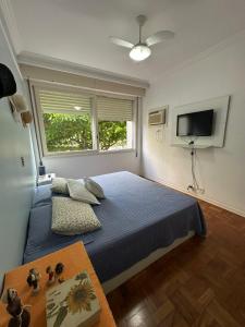 une chambre avec un lit bleu et une télévision dans l'établissement Apartamento Pé na Areia Guarujá Pitangueiras, à Guarujá