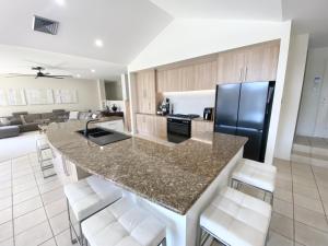 a kitchen with a large island with white bar stools at Emerald Beach Lakefront Luxury Mansion in Emerald Beach