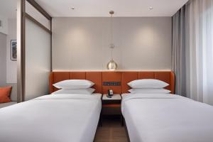 two beds in a hotel room with a desk at Home2 Suite by Hilton Harbin Central Street in Harbin