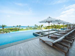 a swimming pool with lounge chairs and umbrellas at The Orion Hotel Motobu Resort & Spa in Motobu