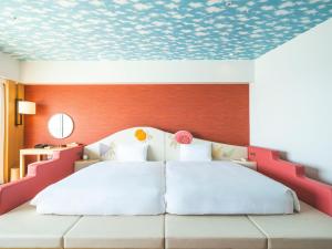 a bedroom with a white bed with a red wall at The Orion Hotel Motobu Resort & Spa in Motobu