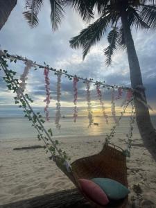 eine Schaukel an einem Strand mit einer Palme in der Unterkunft Trillizas Del Mar Beach Sunset View - Casa Cielo in Tubod
