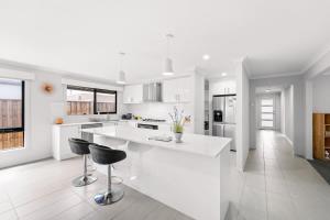 a white kitchen with a counter and two bar stools at Ramlegh Spring Estate - High Quality Family Living in Clyde North