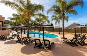 una piscina con sedie, ombrelloni e palme di Praia da Luz - Resort a Luz