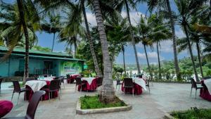 a restaurant with tables and chairs and palm trees at Sakthi River Resort in Pollāchi