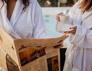 a woman is reading a newspaper and holding a cup and a paper at FRIDA Apartman, Exkluzív várpanorámával, a belváros szívében, ingyenes parkolással in Veszprém