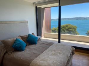 ein Schlafzimmer mit einem Bett mit blauen Kissen und einem großen Fenster in der Unterkunft Departamento Nuevo en Condominio La Puntilla Villarrica in Villarrica