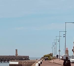 a sidewalk with a pier with a lighthouse in the background at Le Hublot - Maison vue port à Fécamp in Fécamp