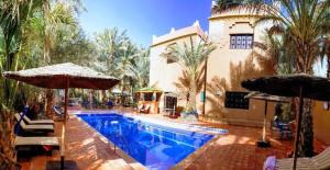 a swimming pool with umbrellas next to a building at Riad le Petit Jardin in Zagora