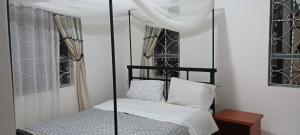 ein Schlafzimmer mit einem Himmelbett mit weißer Bettwäsche und Kissen in der Unterkunft Mara Home 2 in Arusha + 3 Fotos
