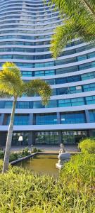 a large building with a palm tree in front of it at Parque do Cais - Flats Premium no Recife por Yolo in Recife