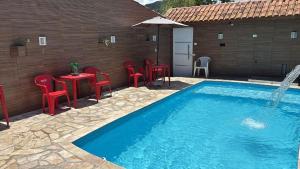 a pool with red chairs and a table with an umbrella at Piscina, Churrasqueira, Ar Condicionado e 3 Vagas de Garagem in Mongaguá