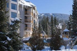 a large building in the snow with trees in front at Ski-In-Out, Pool, Hot Tub, Sauna in Whistler