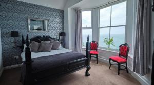 a bedroom with a bed and two red chairs at Beacon Crag in Porthleven