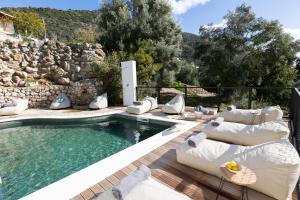 a pool with white furniture and a stone wall at Aella Exclusive Residences Lefkada in Mikros Gialos