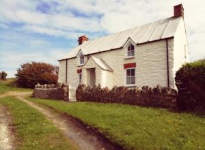 a white house with a stone fence next to a dirt road at Seaside Cottage in HAW
