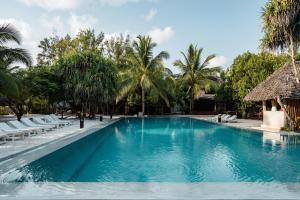a large swimming pool with palm trees and lounge chairs at KUDOS Beach Apartments Jambiani in Jambiani