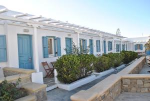 a row of white houses with blue windows and bushes at Petinaros Hotel in Mikonos