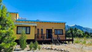 a small yellow house with a porch and a deck at Viento Sur Cabaña in Epuyén