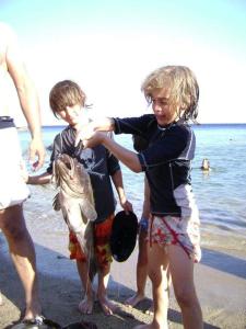three children playing with a fish on the beach at Ikaria Studios in Manganítis