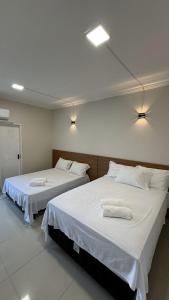 - 2 lits dans une chambre avec des draps blancs et des serviettes dans l'établissement Apartamento frente ao mar na praia do guaibim., à Guaibim