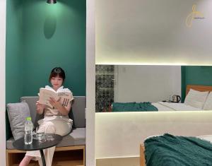 a woman sitting on a couch reading a book in a bedroom at Joi Hospitality - Anthony in Vung Tau