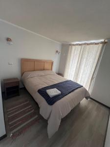 a bedroom with a bed with a blue blanket and a window at Acogedor departamento cerca de avenida del Mar in La Serena