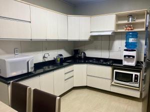 a kitchen with white cabinets and a sink and a microwave at Casa térrea para família no centro de Ametista! in Ametista do Sul
