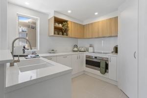 a white kitchen with white cabinets and a sink at Stylish 3-Bed Apartment in Coastal Redcliffe in Redcliffe
