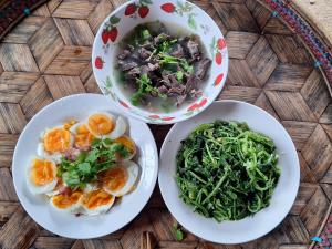 three plates of food on a wooden table with bowls of food at โฮมเสตย์ลาบา1 in Ban Musoe La Ba